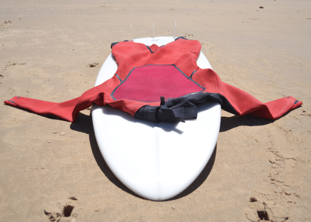 red wetsuit laying on top of white surfboard