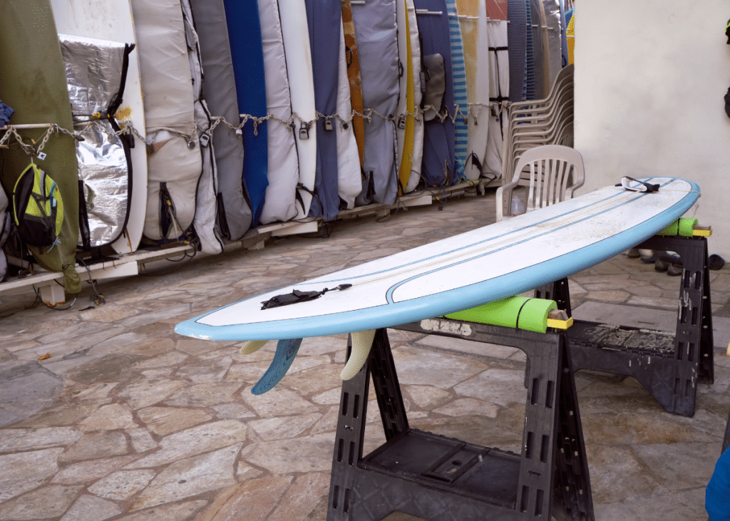 surfboard drying on a rack after being cleaned in front of a rack of surfboards in surf bags for storage