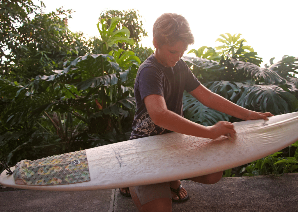 surfer removing surf wax from surfboard by scraping with a plastic tool