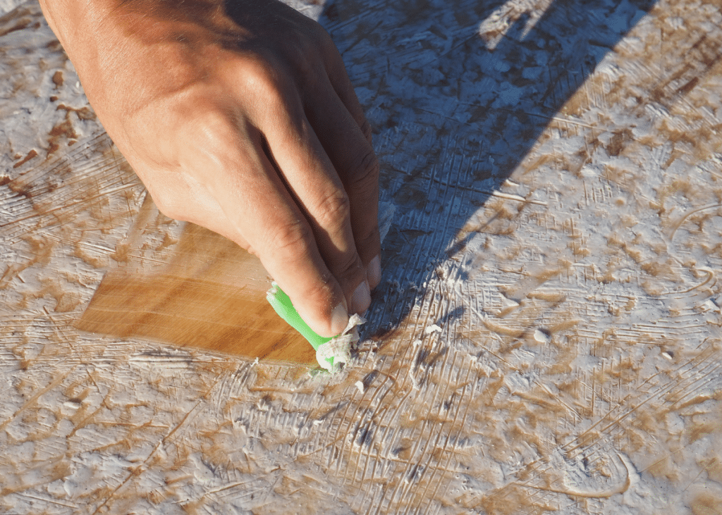 surfer removing surf wax from surfboard by scraping with a plastic tool