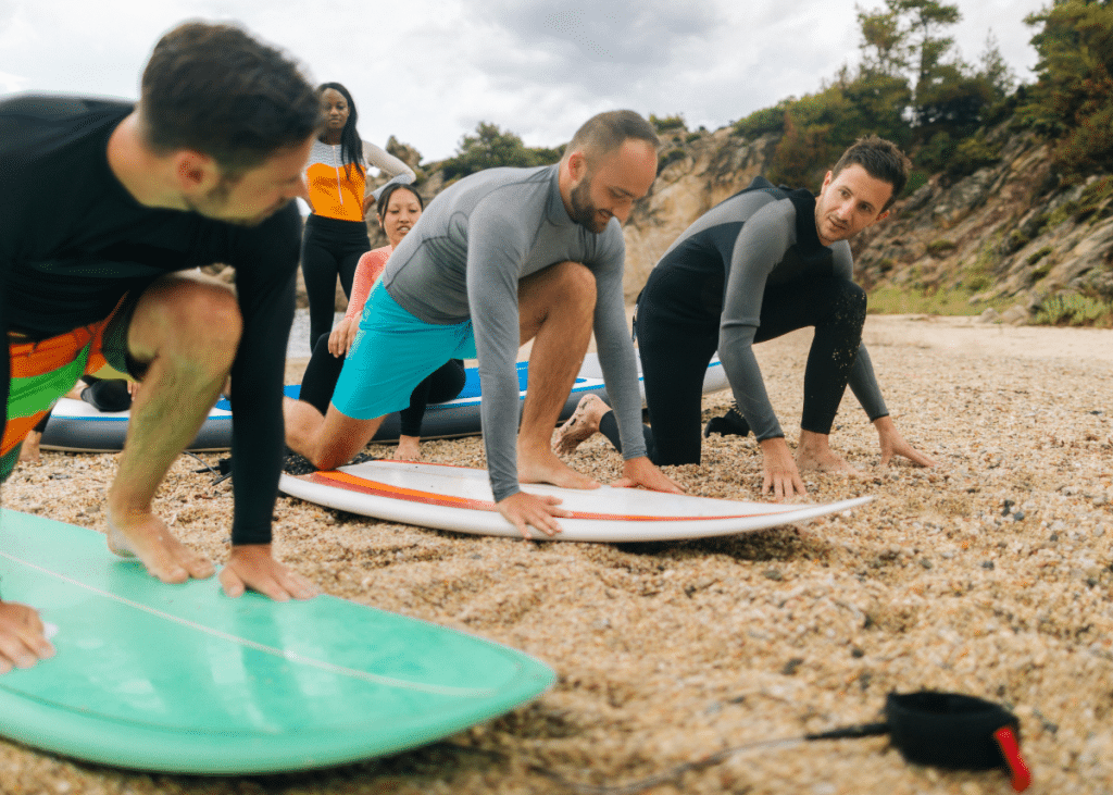 surf instructor showing students how to pop up on a surfboard during a surfing lesson