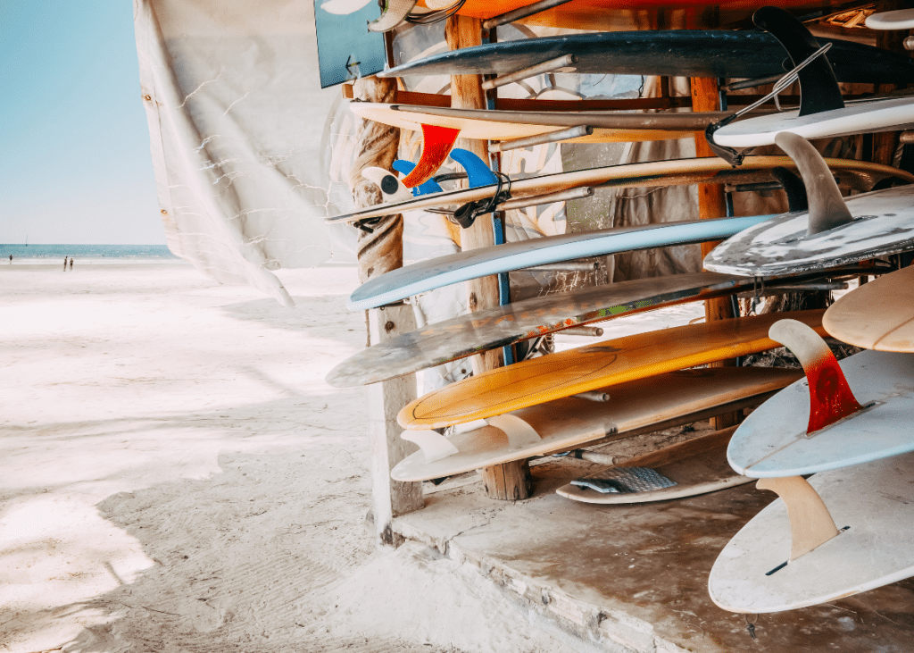 A colorful array of surfboards stacked on a rack at a sandy beach with clear skies and the ocean visible in the background.