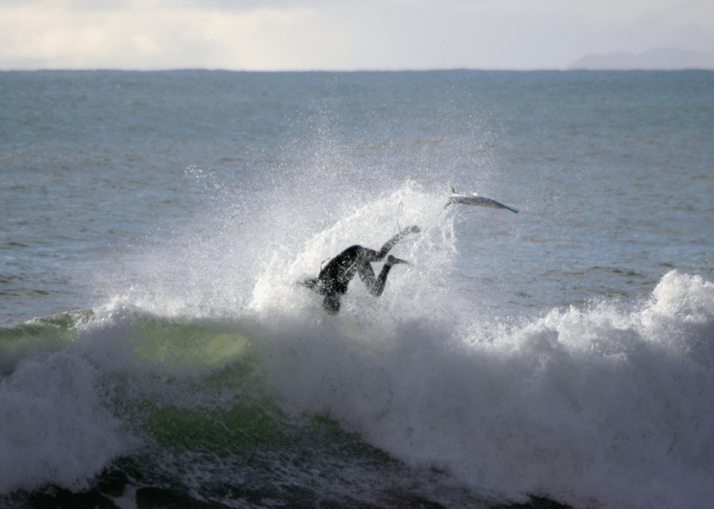 A surfer wipes out dramatically, losing balance and falling off their board amidst a crashing wave in the ocean, looking like a total kook.
