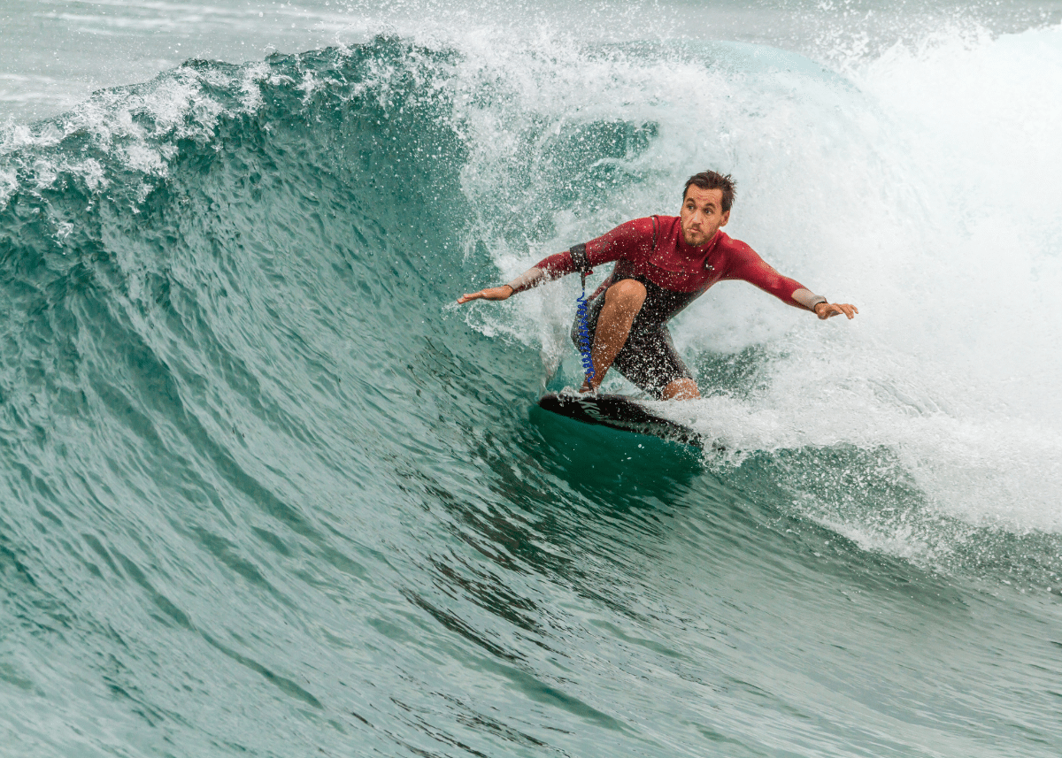 A surfer in a red wetsuit skillfully rides a large, curling ocean wave, with intense concentration visible on his face as he enjoys the thrilling surfing experience.